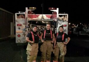 Three firefighters smiling behind a firetruck
