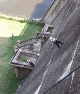 Two people rappelling down a wall